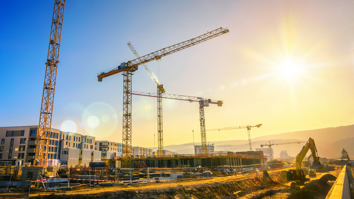 Large construction site including several cranes, with clear sky and the sun